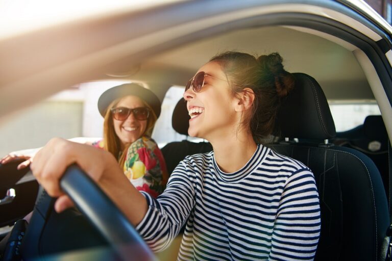Zwei junge Frauen sitzen im Auto und nutzen Trimply für ihre Reiseplanung